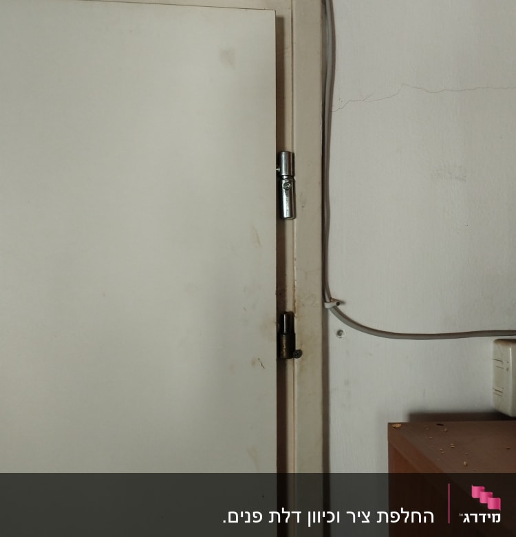 דלת לבנה עם צירים וכבל חשמל ליד